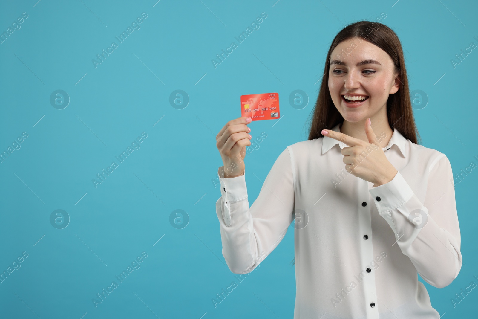 Photo of Happy woman pointing at credit card on light blue background, space for text