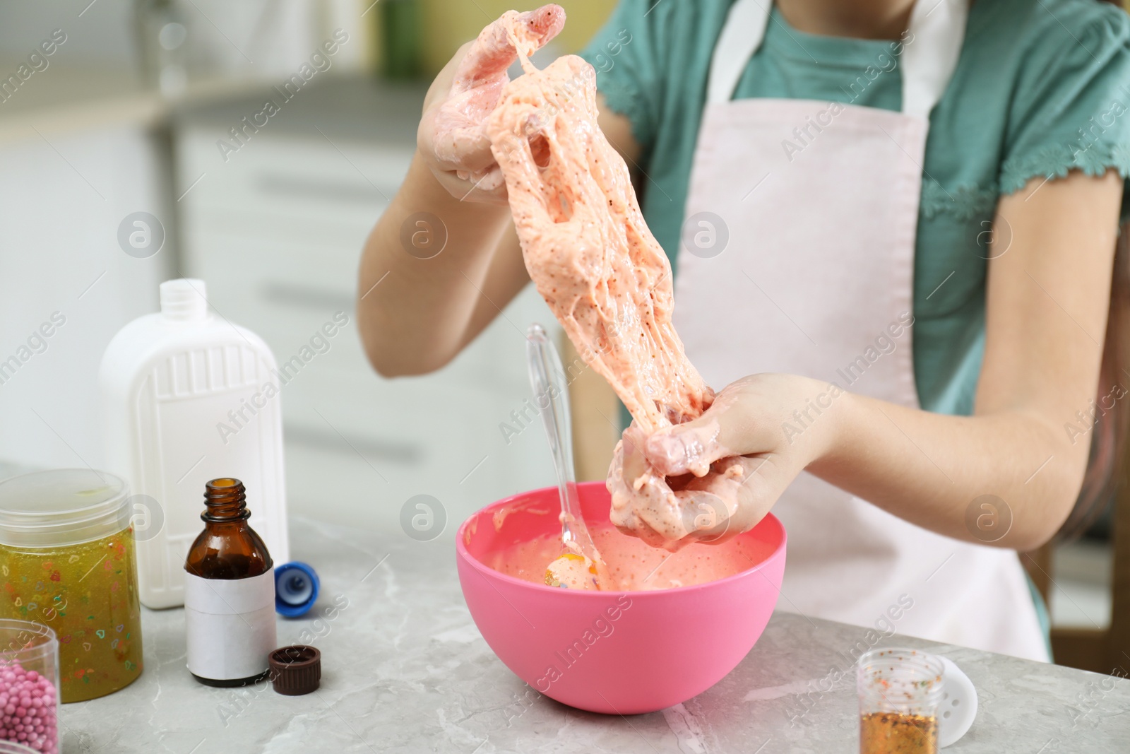 Photo of Little girl kneading DIY slime toy at table in kitchen, closeup