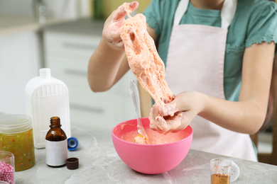 Photo of Little girl kneading DIY slime toy at table in kitchen, closeup