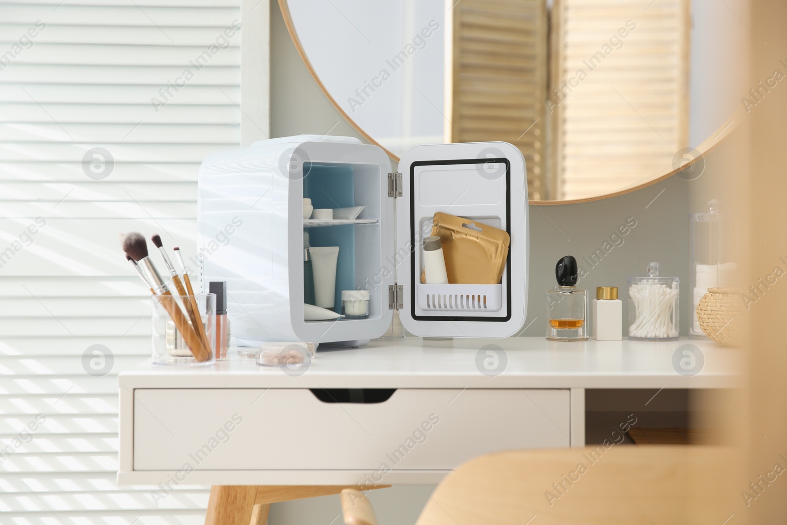 Photo of Cosmetics refrigerator and skin care products on white vanity table indoors