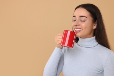 Happy young woman holding red ceramic mug on beige background, space for text