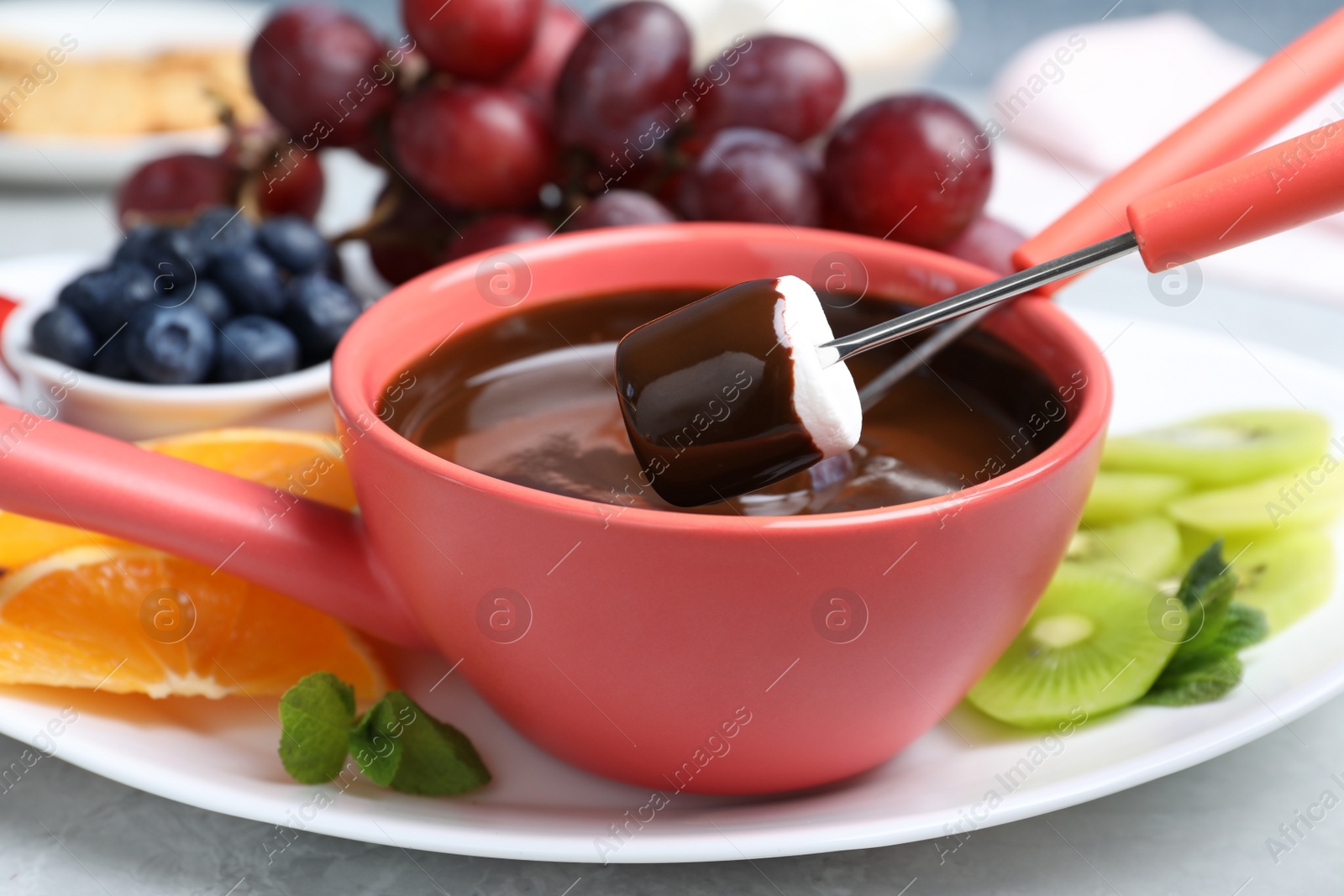 Photo of Dipping marshmallow into pot with chocolate fondue on table, closeup