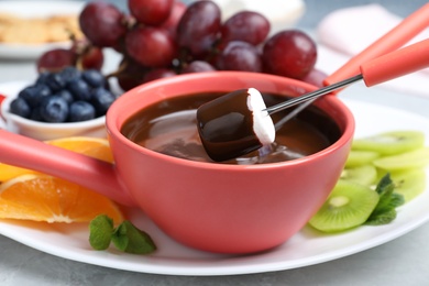 Photo of Dipping marshmallow into pot with chocolate fondue on table, closeup