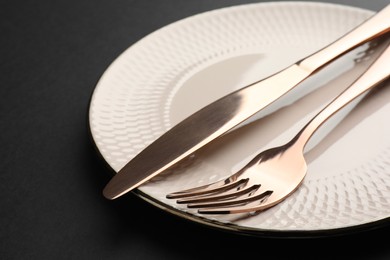 Clean plate, fork and knife on black table, closeup