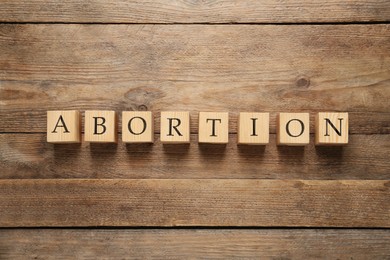 Photo of Word Abortion made of cubes on wooden background, flat lay