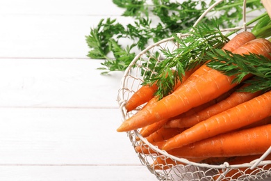 Photo of Basket of carrots on white wooden background. Space for text