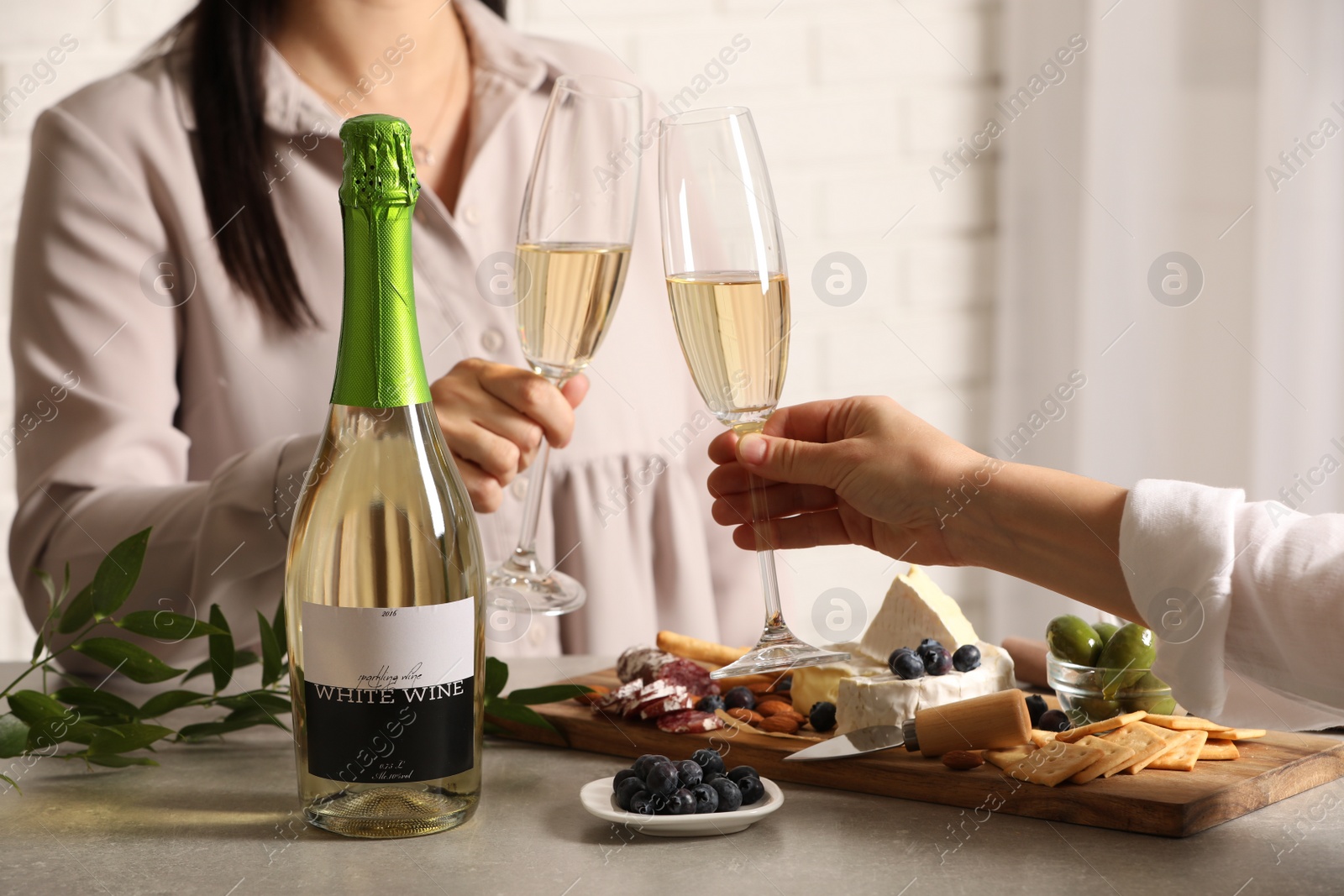 Photo of Women clinking glasses of sparkling wine at table indoors, closeup