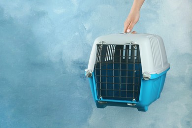 Photo of Woman holding pet carrier against light blue wall, closeup. Space for text
