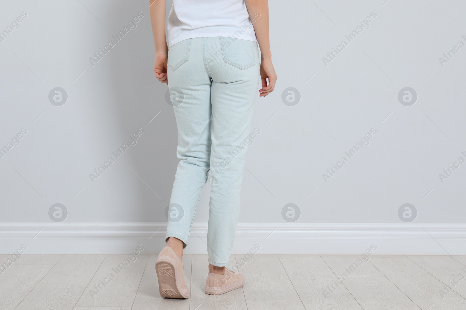 Photo of Young woman in stylish jeans near light wall, closeup