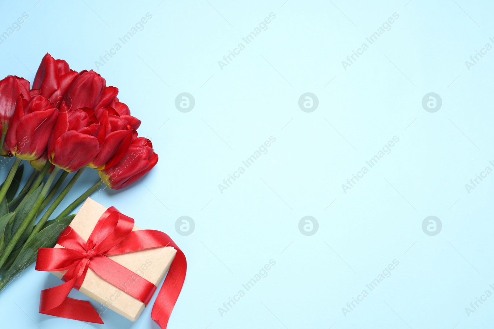 Photo of Beautiful gift box and bouquet of tulip flowers on light blue background, flat lay. Space for text