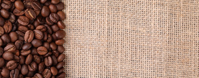 Many coffee beans on burlap fabric, top view. Space for text