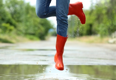 Photo of Woman with red rubber boots jumping in puddle, closeup. Rainy weather