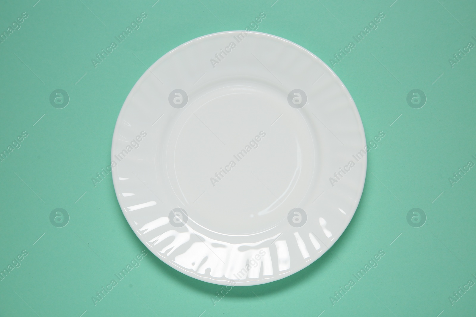 Photo of One white plate on turquoise background, top view