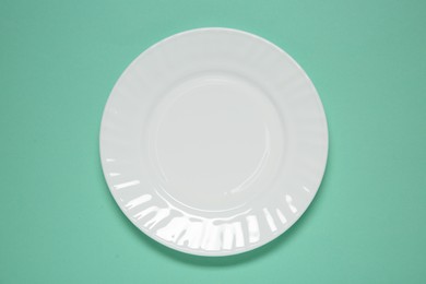 Photo of One white plate on turquoise background, top view