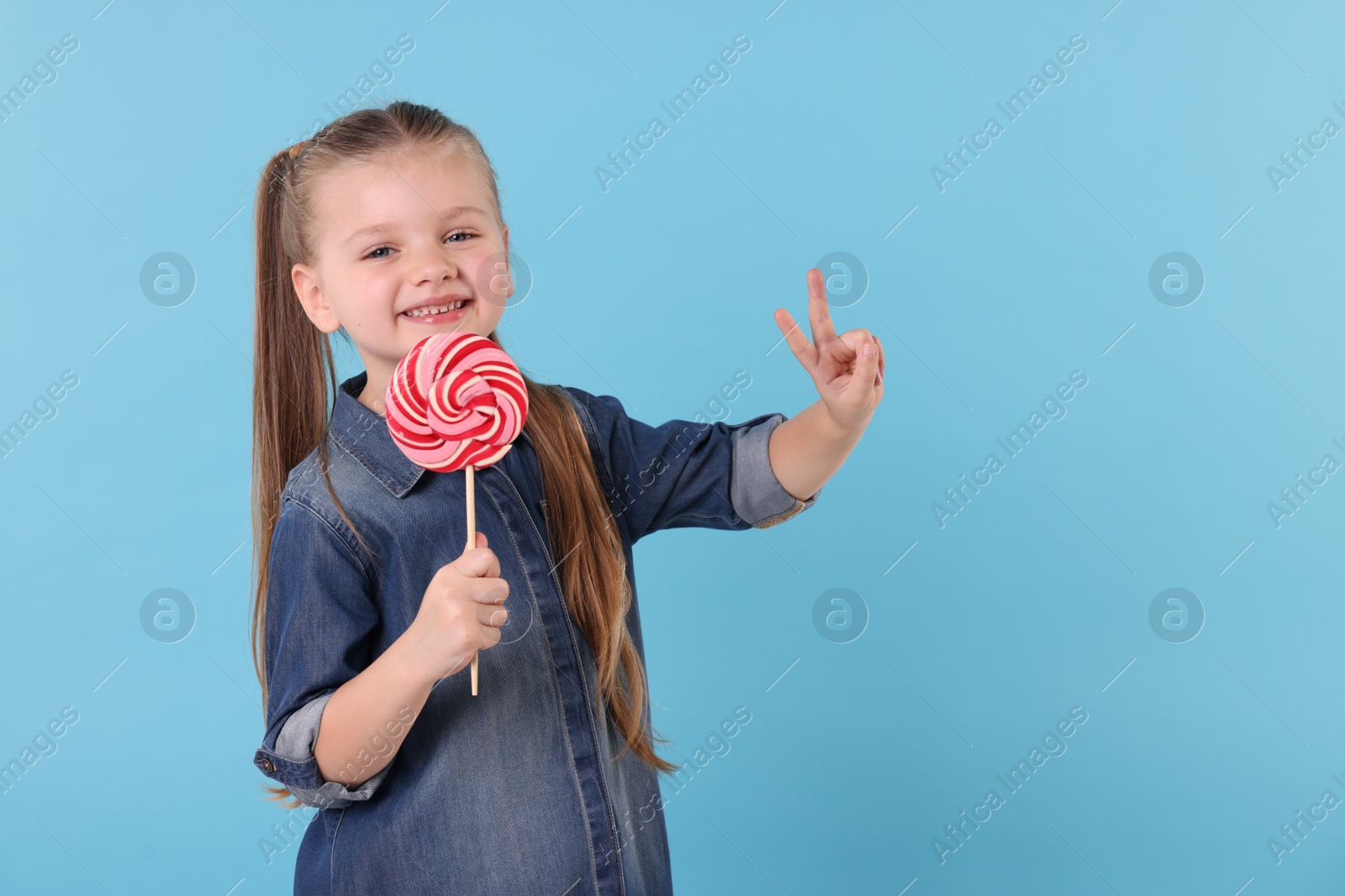 Photo of Happy little girl with bright lollipop swirl on light blue background, space for text