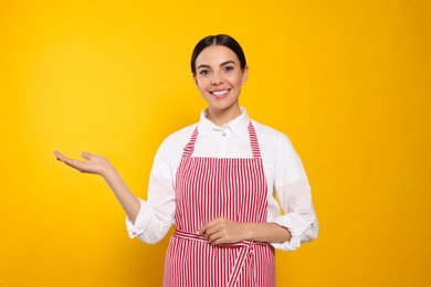 Photo of Young woman in red striped apron on yellow background