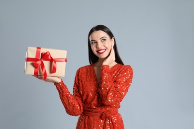 Woman in red dress holding Christmas gift on grey background