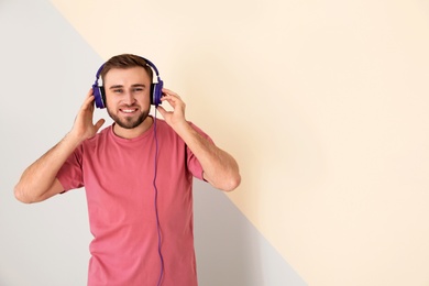 Photo of Handsome man enjoying music in headphones on color background. Space for text