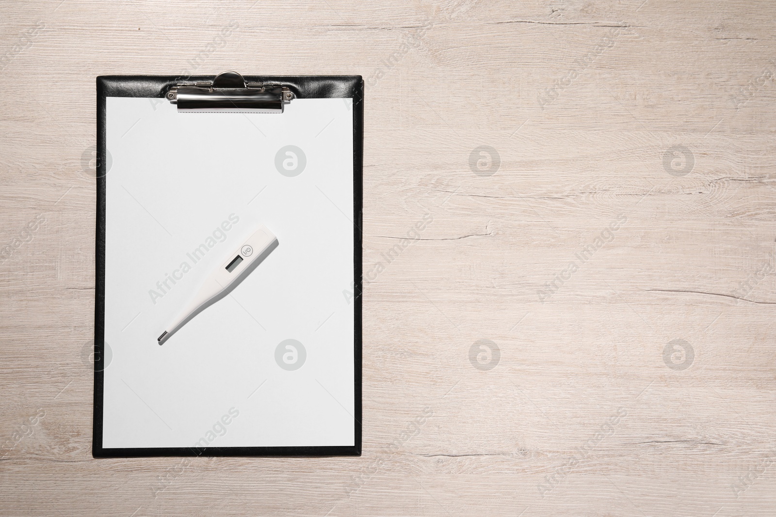 Photo of Clipboard and thermometer on wooden table, top view. Space for text