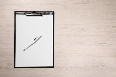 Clipboard and thermometer on wooden table, top view. Space for text