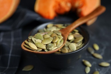 Photo of Bowl with pumpkin seeds and wooden spoon on black table, closeup