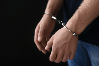 Photo of Man detained in handcuffs against dark background, space for text. Criminal law