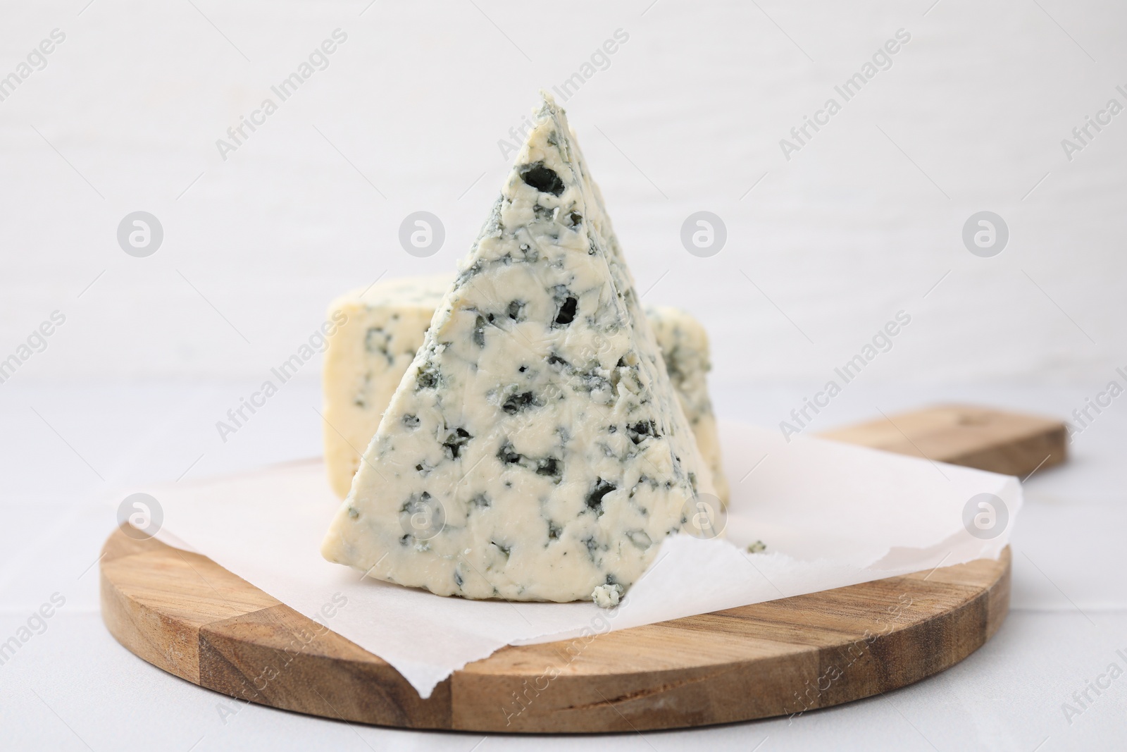 Photo of Wooden cutting board with blue cheese on white tiled table