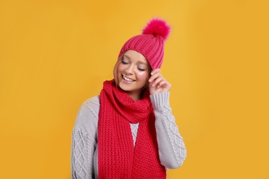 Photo of Young woman in warm sweater, scarf and hat on yellow background. Winter season
