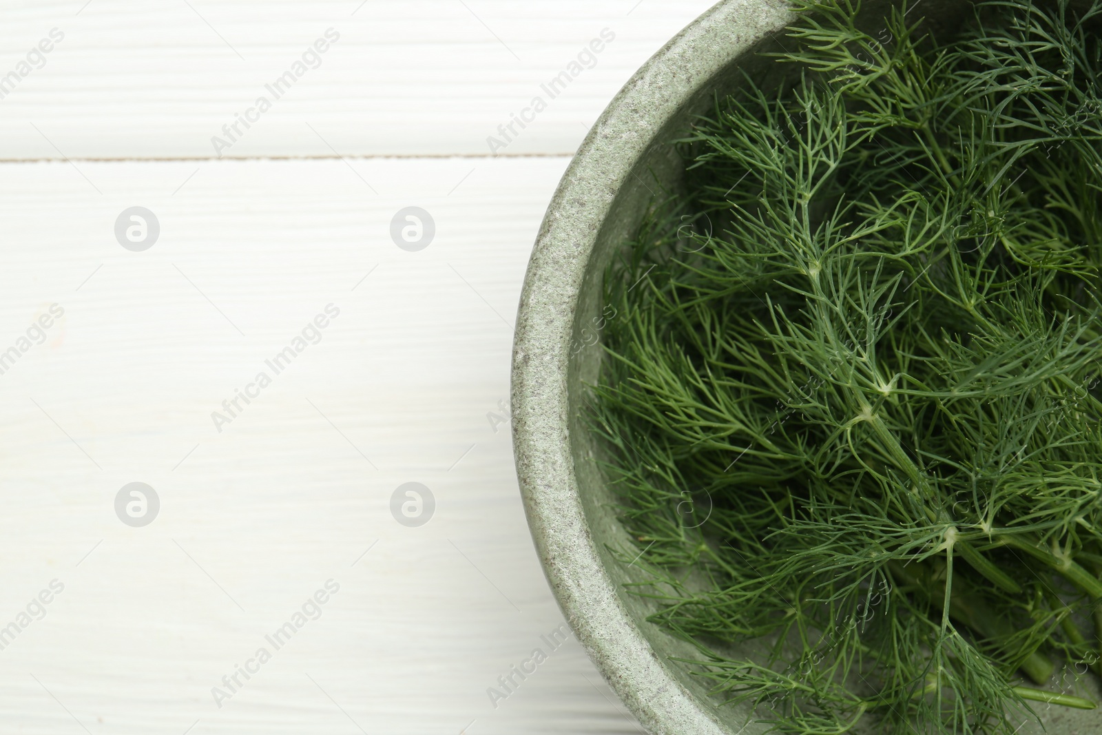 Photo of Bowl of fresh green dill on white wooden table, top view. Space for text