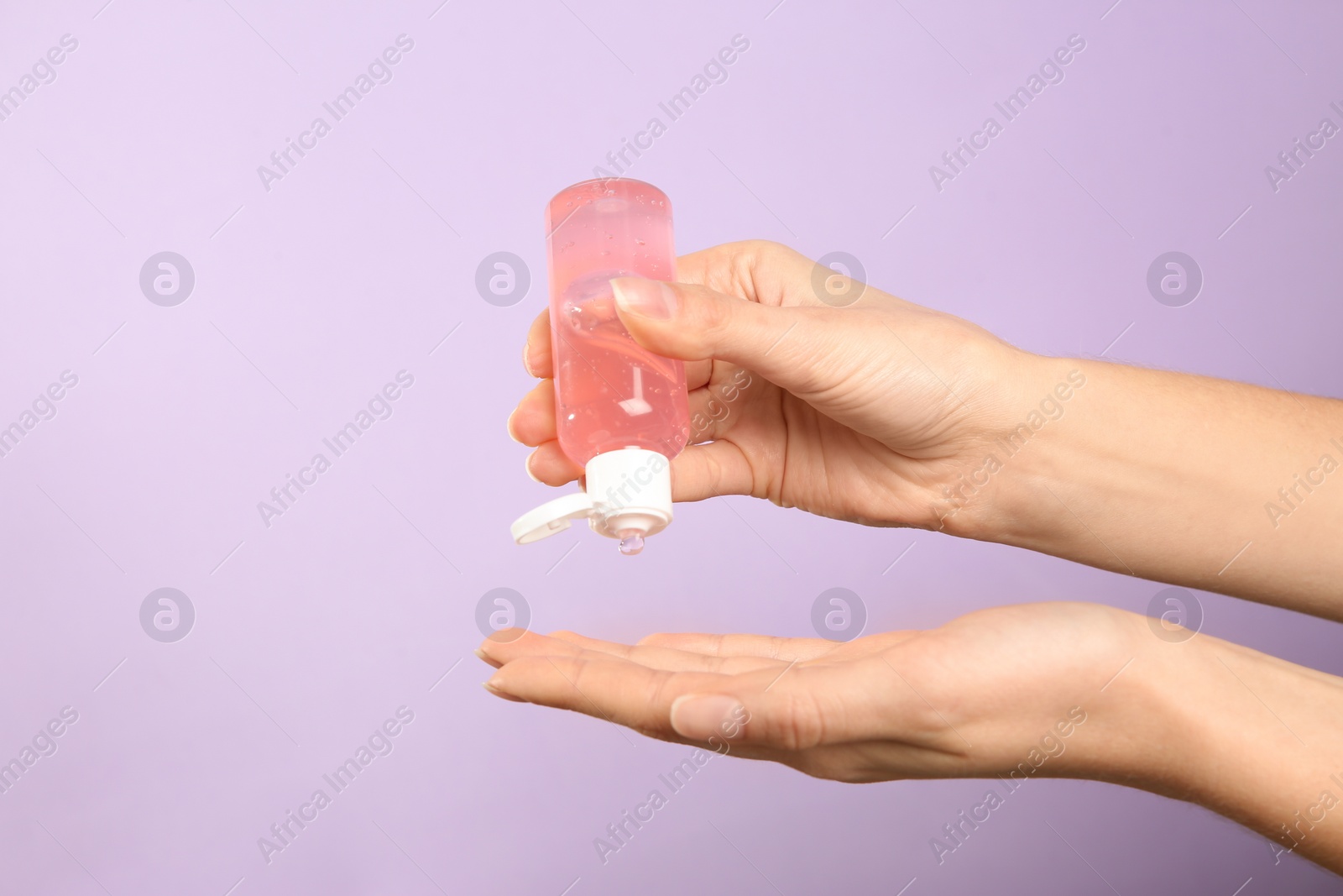Photo of Woman applying antiseptic gel on lilac background, closeup