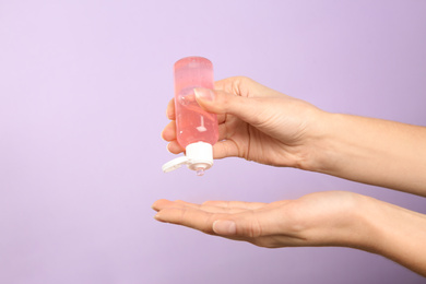 Photo of Woman applying antiseptic gel on lilac background, closeup