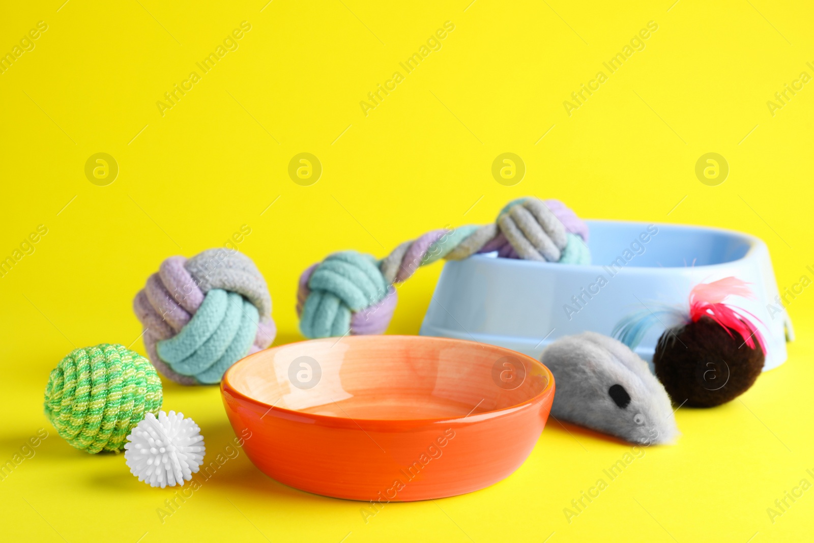 Photo of Feeding bowls and toys for pet on yellow background