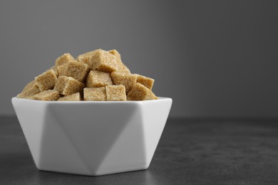 Photo of Brown sugar cubes in bowl on grey table. Space for text