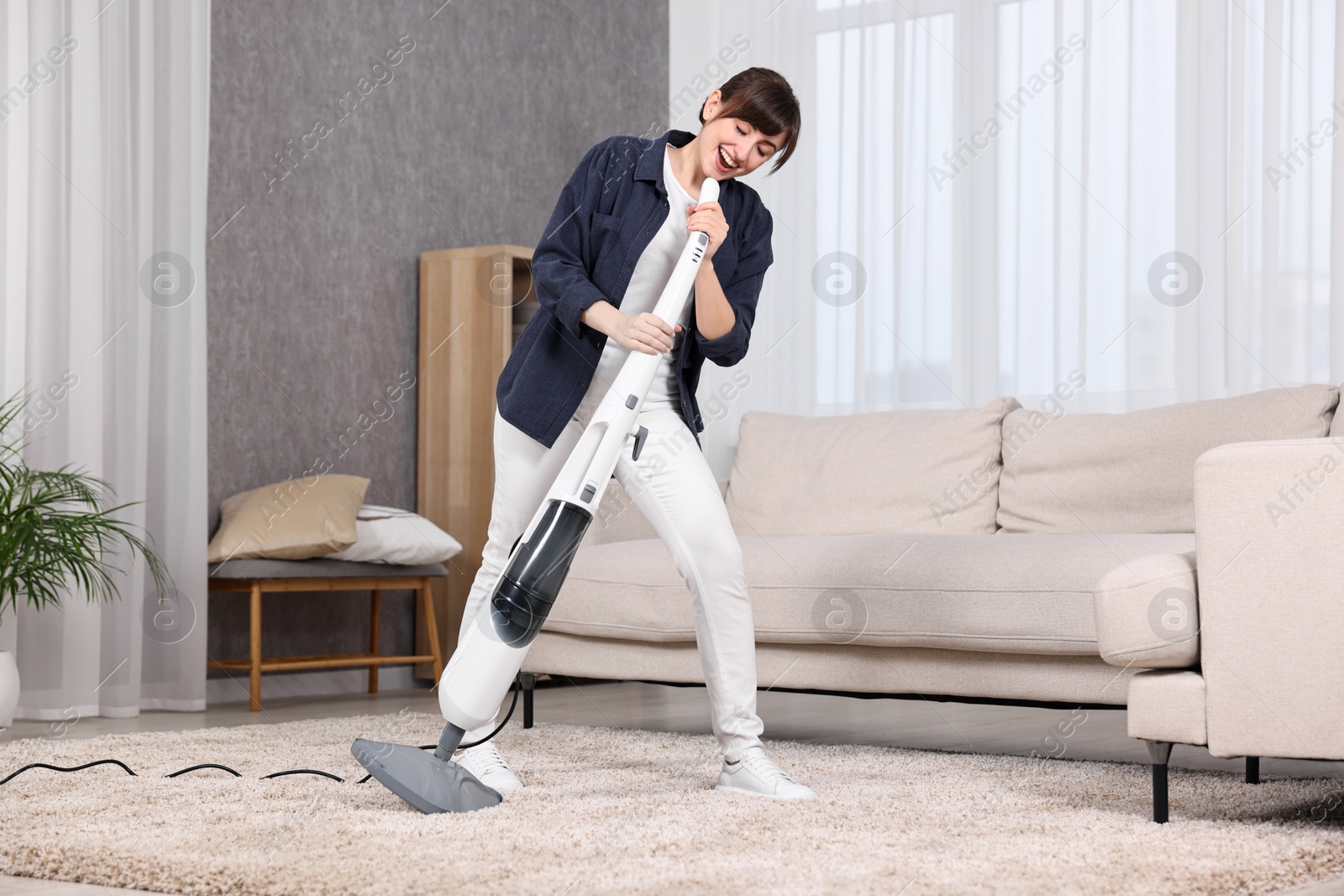 Photo of Happy young housewife having fun while cleaning carpet at home