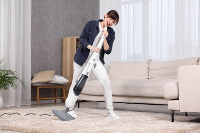 Photo of Happy young housewife having fun while cleaning carpet at home