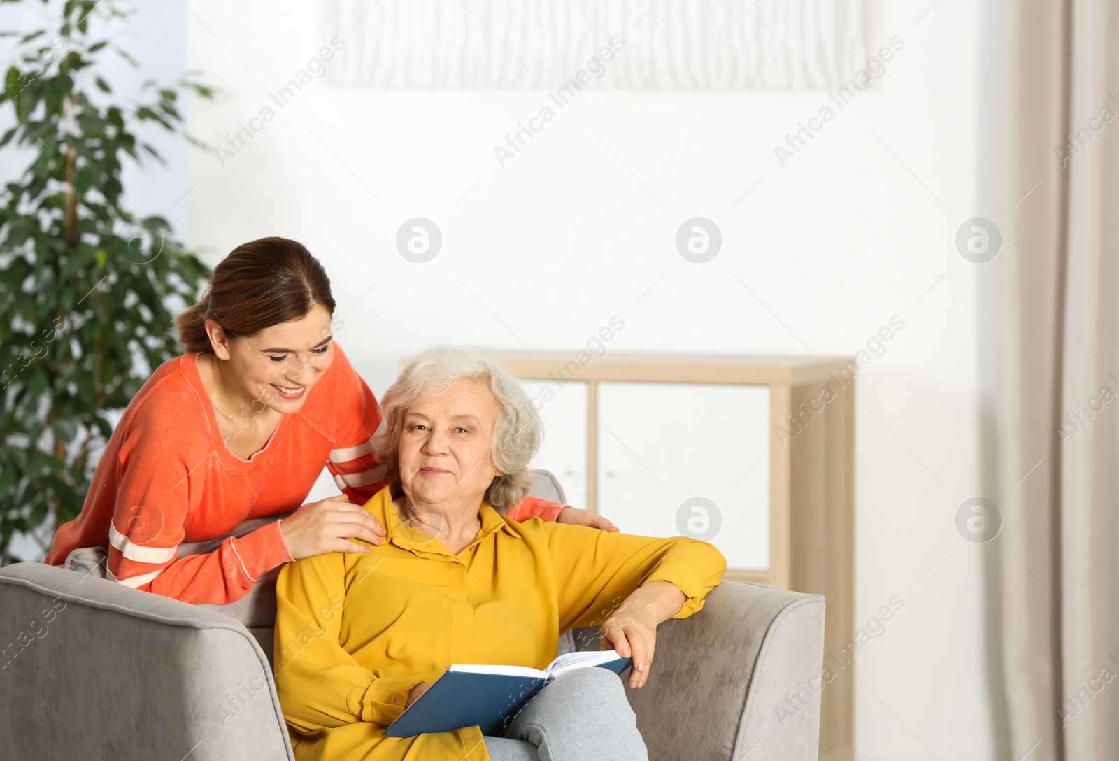Photo of Elderly woman with female caregiver in living room. Space for text