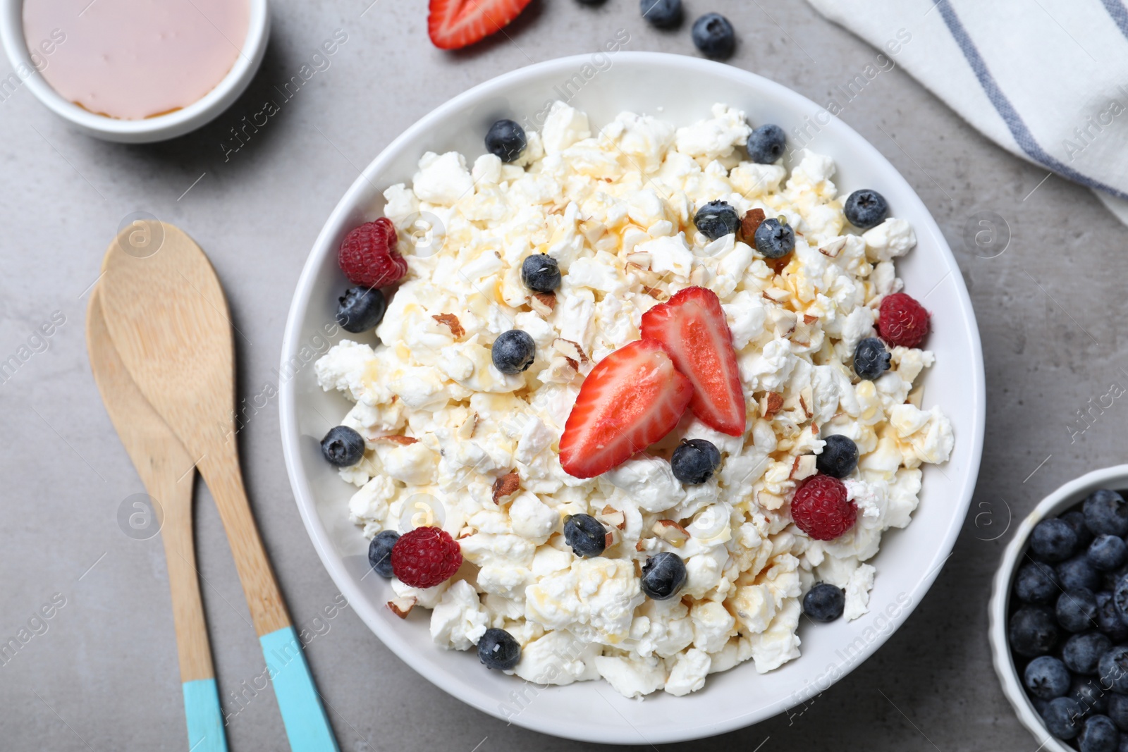 Photo of Delicious cottage cheese with fresh berries and honey served for breakfast on light grey table, flat lay