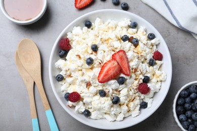 Delicious cottage cheese with fresh berries and honey served for breakfast on light grey table, flat lay