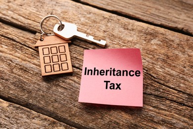 Photo of Inheritance Tax. Paper note and key with key chain in shape of house on wooden table, closeup