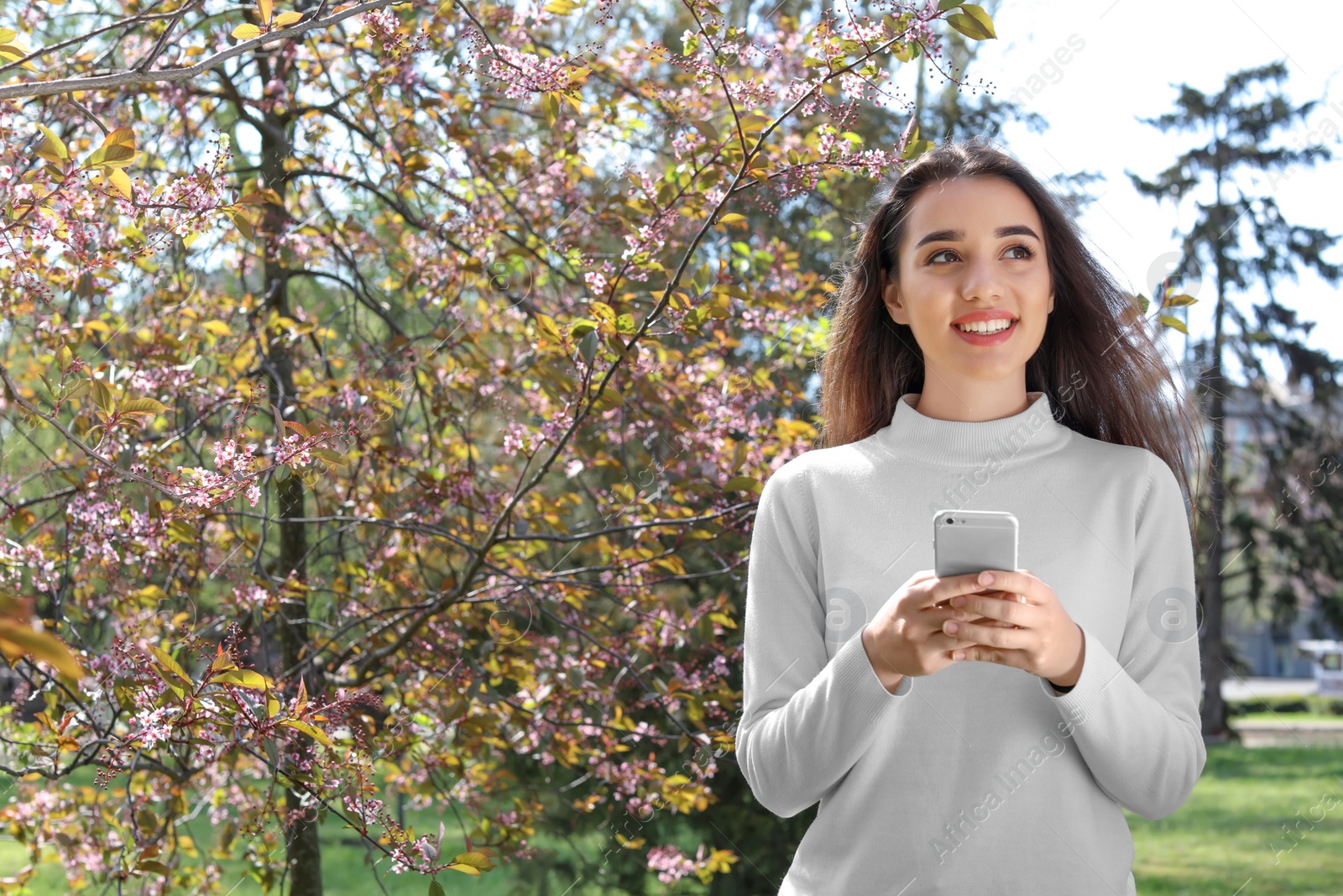 Photo of Young woman using phone outdoors on sunny day