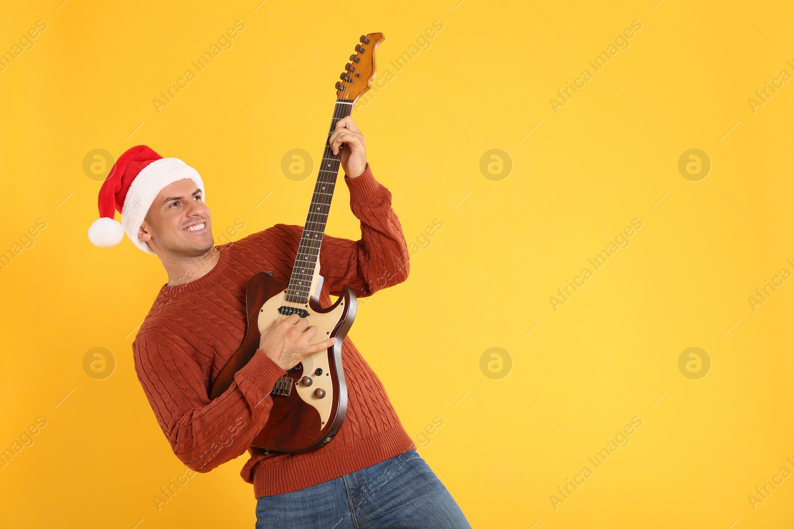 Photo of Man in Santa hat playing electric guitar on yellow background, space for text. Christmas music