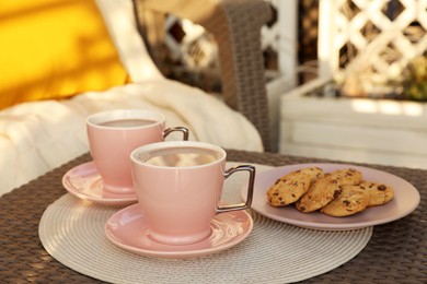 Photo of Cups with tasty cocoa and cookies on rattan table at balcony