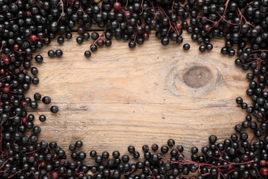 Photo of Frame of black elderberries (Sambucus) on wooden table, flat lay. Space for text