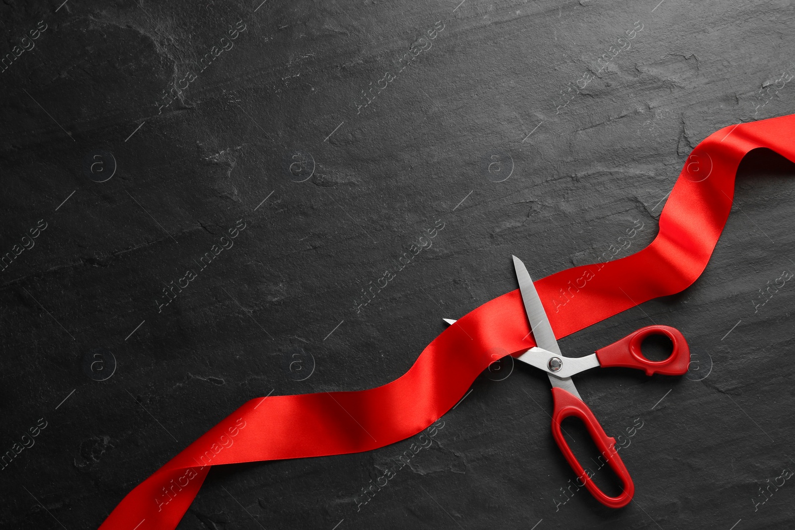 Photo of Red ribbon and scissors on black background, top view. Space for text