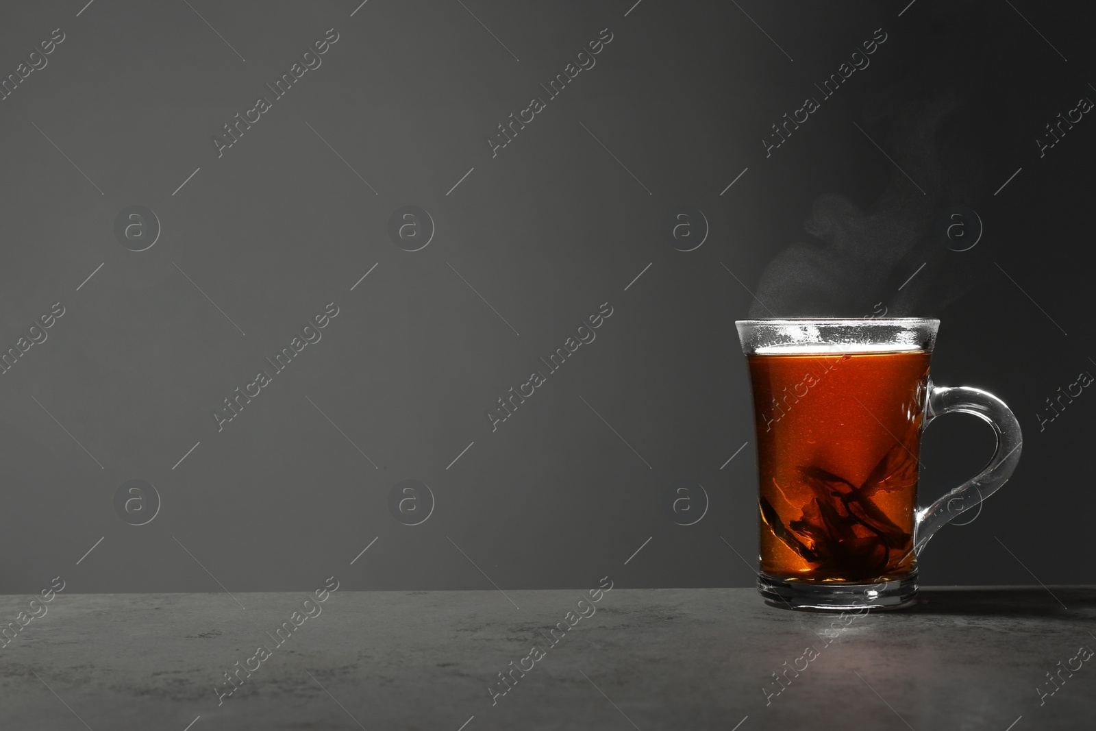 Photo of Glass cup of hot leaf tea on stone table against grey background, space for text