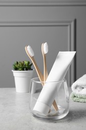 Photo of Bamboo toothbrushes in holder, toothpaste, houseplant and towels on light grey table