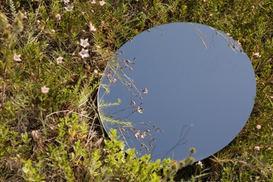 Photo of Spring atmosphere. Round mirror among grass and flowers on sunny day. Space for text