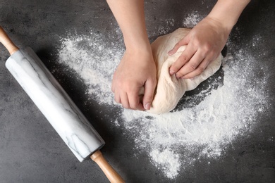 Photo of Female baker preparing bread dough at grey table, top view