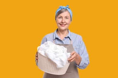 Happy housewife with basket full of laundry on orange background