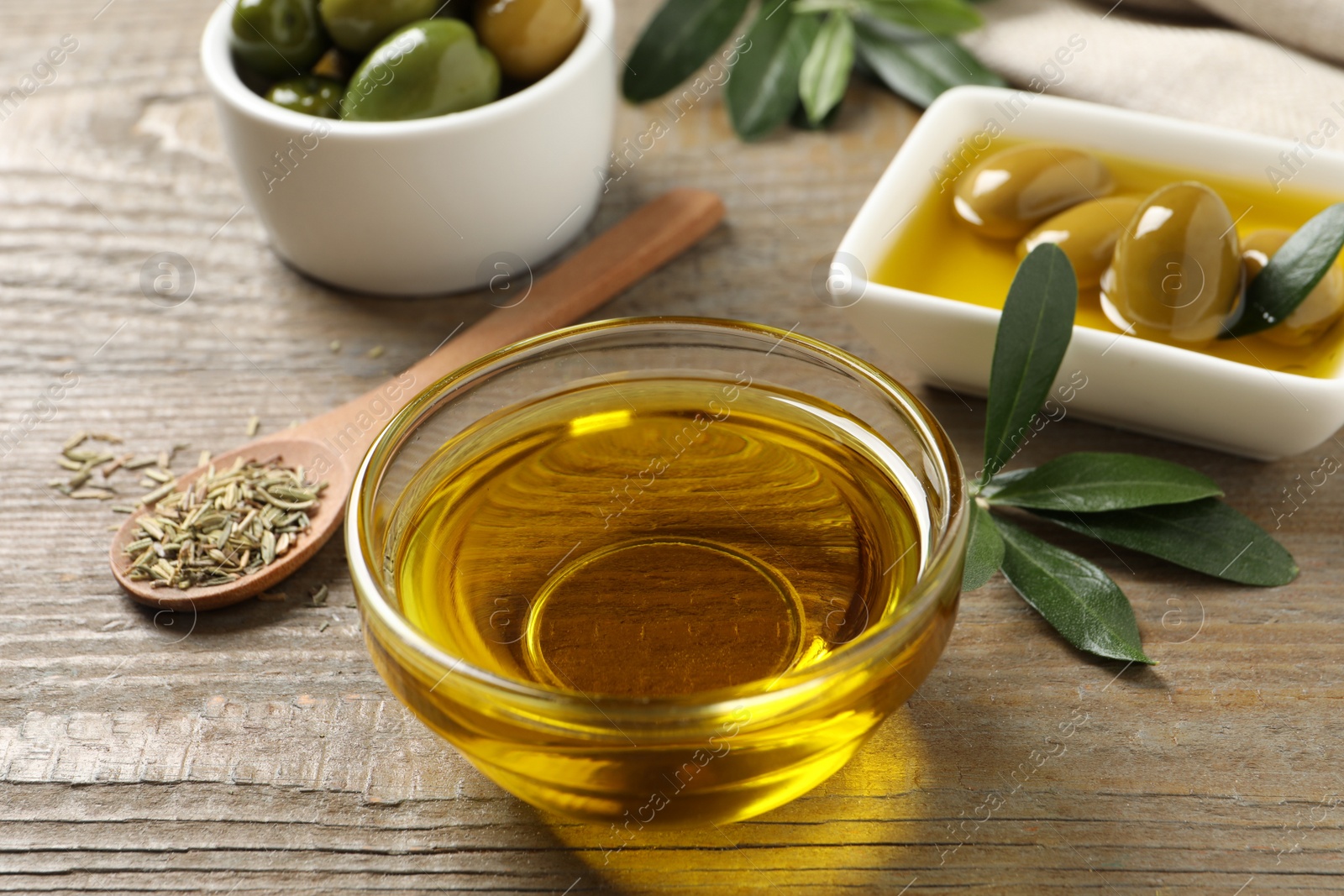 Photo of Fresh oil, ripe olives, dried herb and green leaves on wooden table